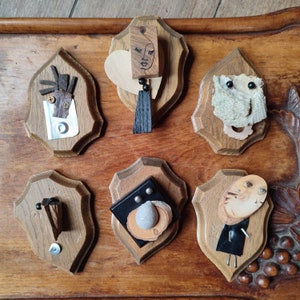Puede incluir: Seis placas de madera con diversas piezas de arte de técnica mixta montadas en ellas. Las placas son de diferentes formas y tamaños y están dispuestas en fila sobre una superficie de madera.