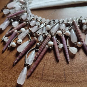 Puede incluir: Un primer plano de un collar de cuentas rosa y blanco con una variedad de formas y tamaños. El collar está hecho de materiales naturales y tiene un estilo bohemio.