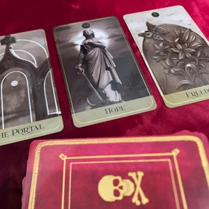 Może przedstawiać: Trzy karty tarota na czerwonym aksamitnym tle. Karty pochodzą z talii zwanej "The Shadowscapes Tarot". Karty to "The Portal", "Hope" i "Freedom".