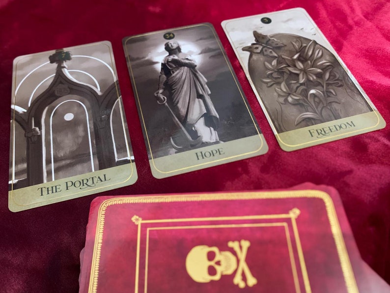 Może przedstawiać: Trzy karty tarota na czerwonym aksamitnym tle. Karty pochodzą z talii zwanej "The Shadowscapes Tarot". Karty to "The Portal", "Hope" i "Freedom".