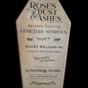 Może przedstawiać: Beżowe pudełko w kształcie trumny z czerwoną obw&oacute;dką. Pudełko ma vintage'owy wygląd i zawiera tekst "Roses & Dust & Ashes" w czarnym piśmie. Tekst "An oracle featuring Cemetery Symbols" r&oacute;wnież jest w kolorze czarnym. Tekst "Written by Stacey Williams-Ng Beloved Wife & Mother" r&oacute;wnież jest w kolorze czarnym. Tekst "Illustrated by the Authoress" r&oacute;wnież jest w kolorze czarnym. Tekst "La Panthere Studio 2023 - First Edition Printing" r&oacute;wnież jest w kolorze czarnym.