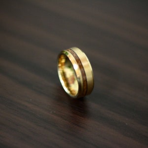May include: A gold ring with a brown wood inlay. The ring is on a dark wood surface.