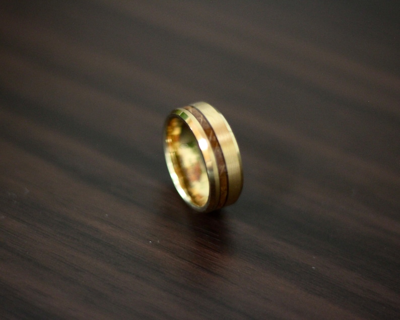 May include: A gold ring with a brown wood inlay. The ring is on a dark wood surface.