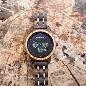 Puede incluir: Un reloj de pulsera de madera negro y marr&oacute;n con una esfera de cron&oacute;grafo. La esfera del reloj tiene un fondo negro con marcas blancas y acentos verdes. El nombre de la marca "AxMen" est&aacute; impreso en la esfera del reloj.