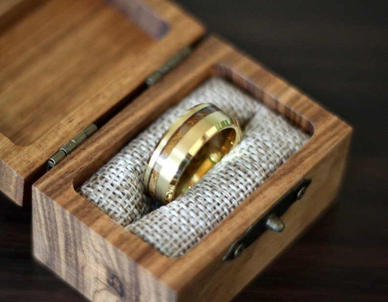 May include: A gold ring with a wooden inlay is displayed in a wooden ring box with a burlap lining.