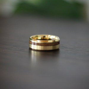 May include: A gold ring with a wooden inlay. The ring has a polished finish and a beveled edge.