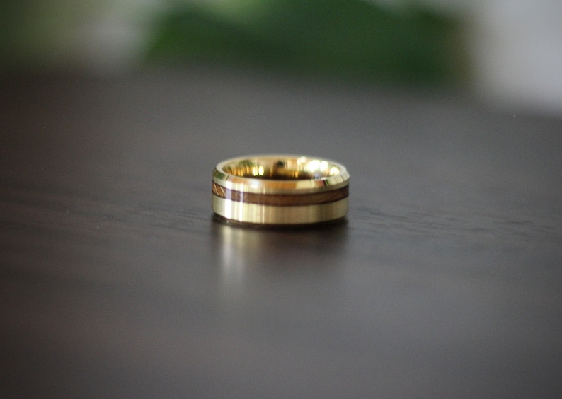 May include: A gold ring with a wooden inlay. The ring has a polished finish and a beveled edge.
