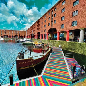 May include: A red and white boat named "France-Hayhurst" is docked at a waterfront with a colorful striped walkway leading to a brick building with arched doorways.