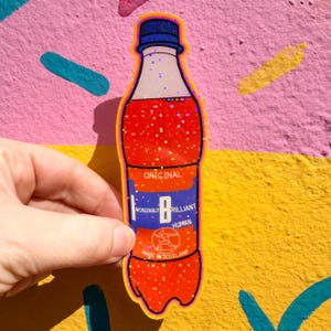 May include: A holographic sticker of a plastic bottle filled with orange liquid. The label features the text ORIGINAL, INCREDIBLY BRILLIANT HUMAN, and MADE IN SCOTLAND, along with a circular graphic of a figure throwing a discus.