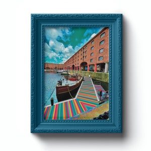 May include: A blue framed photograph of a boat docked in a harbor with a colorful striped walkway leading to the boat. The boat is brown and white with the name "France" written on the side. The harbor is lined with brick buildings.