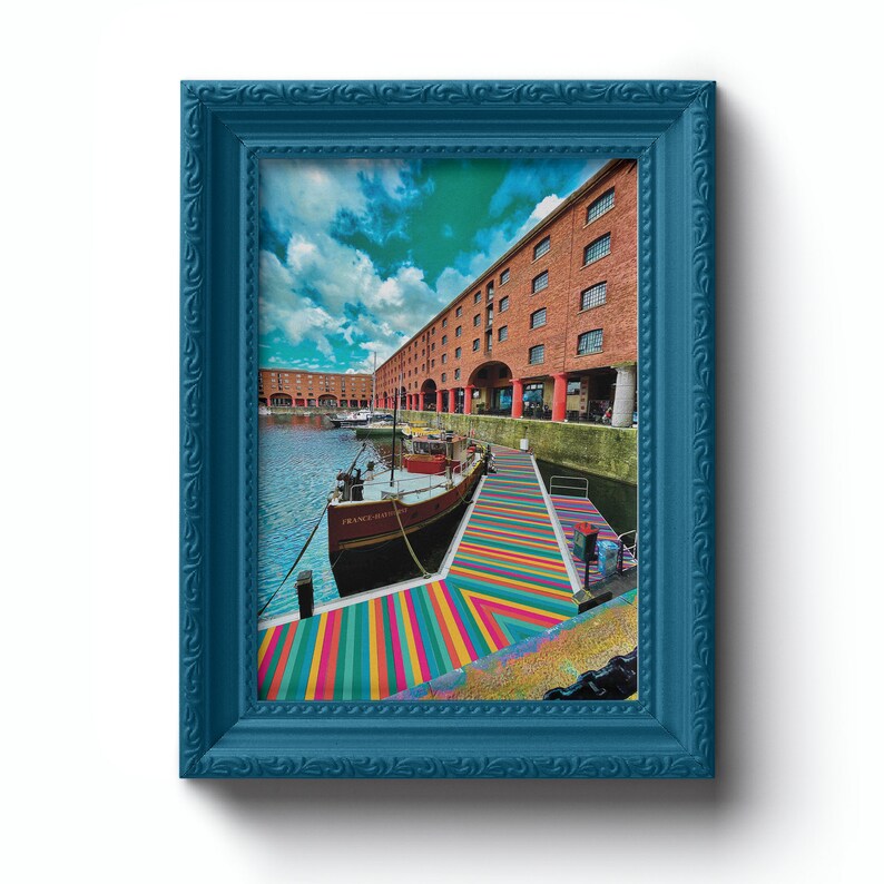 May include: A blue framed photograph of a boat docked in a harbor with a colorful striped walkway leading to the boat. The boat is brown and white with the name "France" written on the side. The harbor is lined with brick buildings.