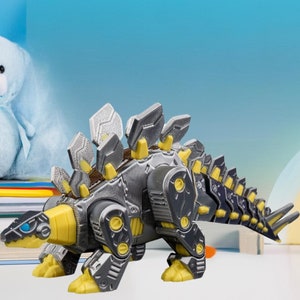 May include: A gray and yellow robotic dinosaur toy with a spiky back and a long tail. The toy is posed on a white surface with a blue background.