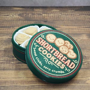 Puede incluir: Una lata redonda verde de galletas de mantequilla, con la tapa parcialmente abierta. La tapa presenta las palabras "Shortbread Cookies" y un gráfico de galletas sonrientes. La lata está sobre una superficie de madera.