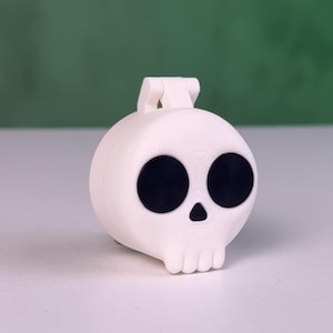 Peut inclure: Un récipient en plastique blanc en forme de crâne avec un couvercle à charnière. Le crâne a des yeux noirs et un petit nez.