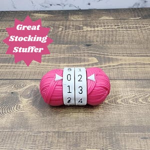 May include: A pink yarn ball with two white plastic counter rings. The rings have numbers 0, 1, 2, 3, 4, and 9 printed on them.