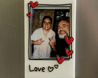 May include: White photo frame with a black border and red hearts around the edges. The frame has a photo of two people smiling and making peace signs. The text "Love" is written below the photo.