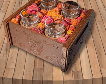 May include: A wooden shot glass holder with a carved skull design. The holder contains four clear shot glasses surrounded by colorful, decorative flowers. The wood is stained brown, and the flowers are red, orange, and yellow.