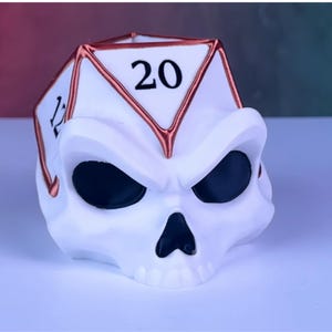 May include: White skull-shaped dice holder with a 20-sided die on top. The die is copper-colored with black numbers. The skull has black eyes and a black nose.