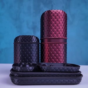 Pode incluir: Uma variedade de recipientes e bandejas decorativas em tons de preto e bordô. Os recipientes têm um padrão texturizado e tecido, e as bandejas são ovais e retangulares. O fundo é um gradiente de azul.