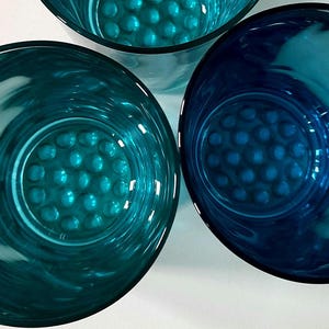 Pode incluir: Três copos de bebida verde-azulado. Os copos têm formato redondo com um padrão texturizado e pontilhado na base. Os copos são feitos de um material transparente. Os copos estão vazios.