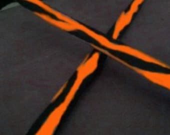 May include: Two crossed drumsticks with a black and orange tiger stripe pattern. The drumsticks are angled across each other against a dark gray background. The orange stripes are thick and vibrant.