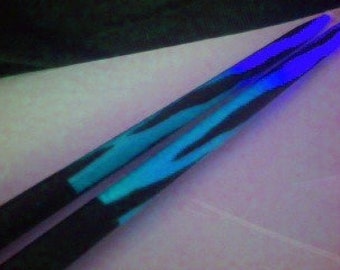 May include: A pair of black drumsticks with a blue and black gradient design. The drumsticks are painted with a tiger stripe pattern.