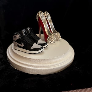 May include: A white ceramic pedestal with a pair of black and white sneakers and a pair of red high heels with silver accents.