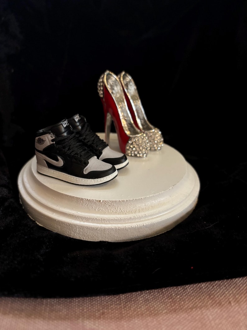 May include: A white ceramic pedestal with a pair of black and white sneakers and a pair of red high heels with silver accents.