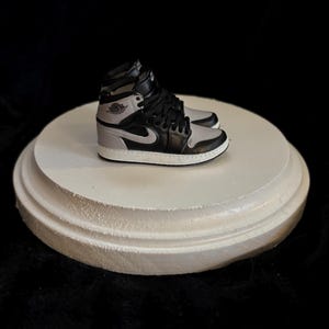 May include: A pair of black and grey sneakers with a white sole. The sneakers are on a white circular display stand.