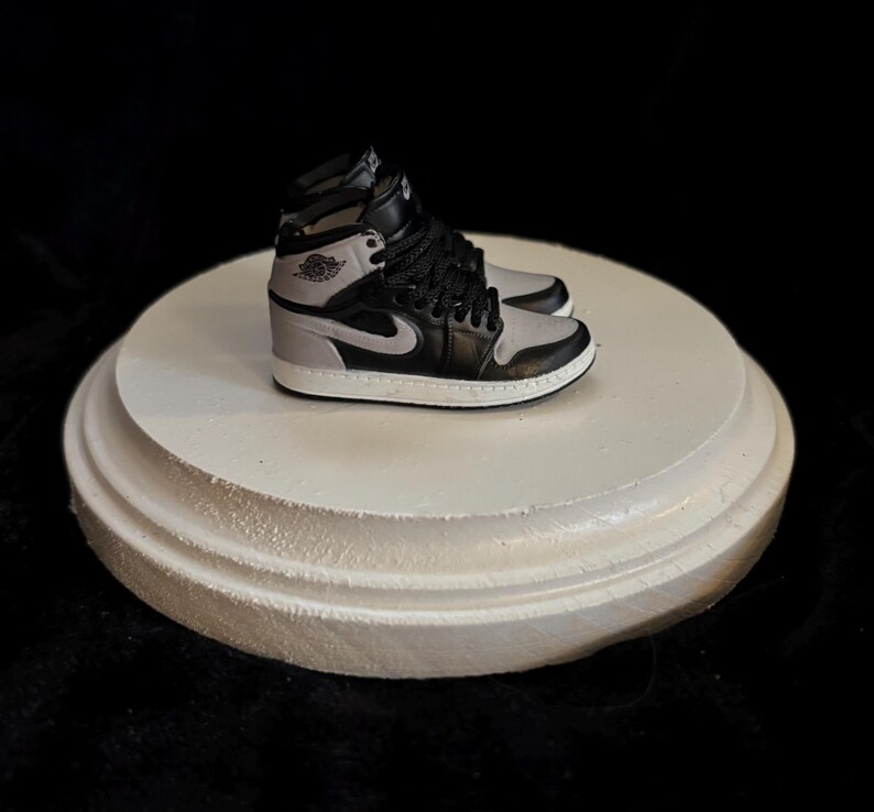 May include: A pair of black and grey sneakers with a white sole. The sneakers are on a white circular display stand.