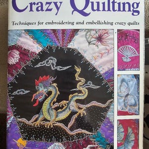 May include: A softcover book titled Motifs for Crazy Quilting by J. Marsha Michler. The cover features a large central embroidered dragon on a black background, surrounded by colorful fabric patches and three smaller panels showing fan, butterfly, and leaf motifs.