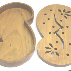 May include: Two wooden trays, one with a carved design and the other plain, are shaped like the number eight. The carved tray has a floral design and small holes.