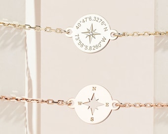 May include: Three silver bracelets with compass charms. The charms feature coordinates and a compass rose. The top bracelet has the coordinates "40.476.3276°N 73.581.5260°W", the middle bracelet has a compass rose, and the bottom bracelet has the coordinates "37.773972 -122.431297".
