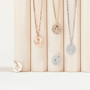 May include: Five silver and gold necklaces with delicate floral pendants. Each pendant features a different flower design and is engraved with a name. The necklaces are displayed on a white background.