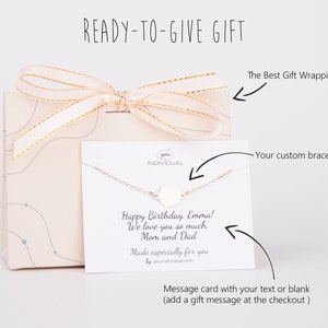 Puede incluir: Una caja de regalo con una cinta rosa y una tarjeta blanca con una pulsera de plata y un mensaje que dice "Feliz cumplea&ntilde;os, Emma! Te queremos mucho. Mam&aacute; y Pap&aacute;. Hecho especialmente para ti por youindividual.com".
