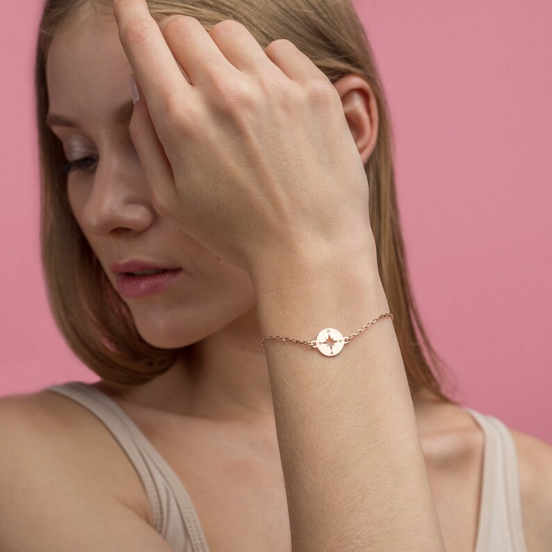 May include: A delicate gold bracelet with a compass charm. The charm is a circle with a compass rose design cut out of the center.