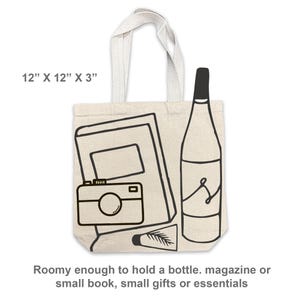 May include: Beige tote bag with black line art of a camera, notebook, bottle, and tube. The bag measures 12" x 12" x 3" and has a cream-colored handle. Text on the bag says "Roomy enough to hold a bottle. magazine or small book, small gifts or essentials."