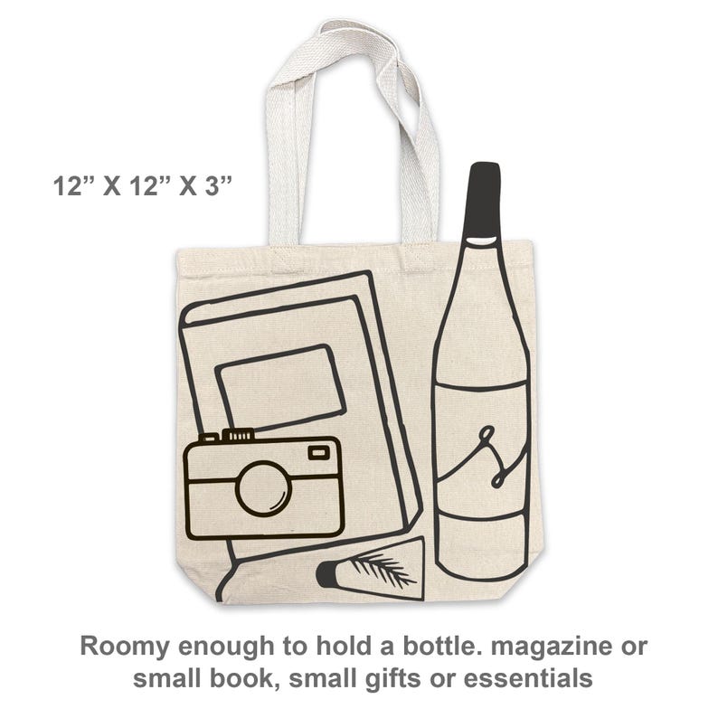 May include: Beige tote bag with black line art of a camera, notebook, bottle, and tube. The bag measures 12" x 12" x 3" and has a cream-colored handle. Text on the bag says "Roomy enough to hold a bottle. magazine or small book, small gifts or essentials."