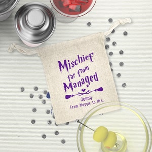 May include: A small, white fabric bag with a purple design that says "Mischeif Far From Managed" with a heart and two broomsticks. The bag has a drawstring closure and is perfect for a small gift or favor. The text below the design says "Jenny From Muggle to Mrs."