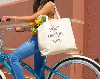 May include: A woman in a straw hat and blue jeans rides a blue bicycle with a white tote bag that says "your design here".