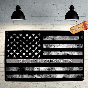 May include: Black and white American flag with a thin gray stripe across the middle. The text "CPL DAN KRIEGBAUM" is printed on the gray stripe.