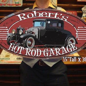 May include: A rusty oval-shaped metal sign with a red background and white lettering. The sign features a black hot rod car with a checkered pattern on the hood. The text on the sign reads "Robert's Hot Rod Garage" and "15" Tall x 30" Long".
