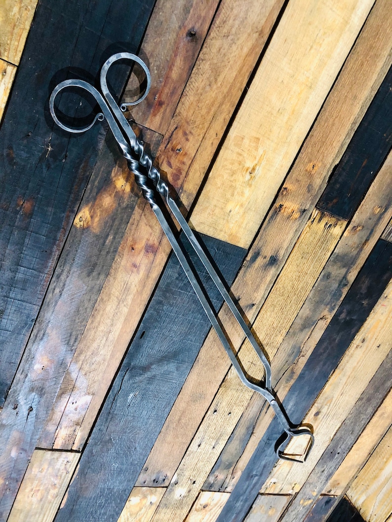 May include: A pair of black metal fireplace tongs with a twisted handle and a heart-shaped design at the end.