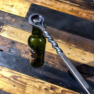 May include: A metal bottle opener with a twisted handle is used to open a green glass bottle of Sonoma Cider.