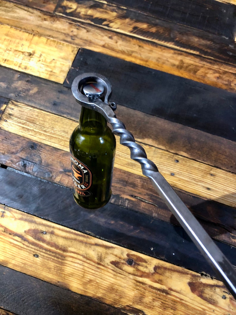 May include: A metal bottle opener with a twisted handle is used to open a green glass bottle of Sonoma Cider.