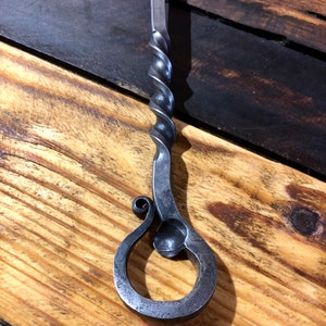 May include: A hand-forged bottle opener with a twisted metal handle and a decorative loop at the end.