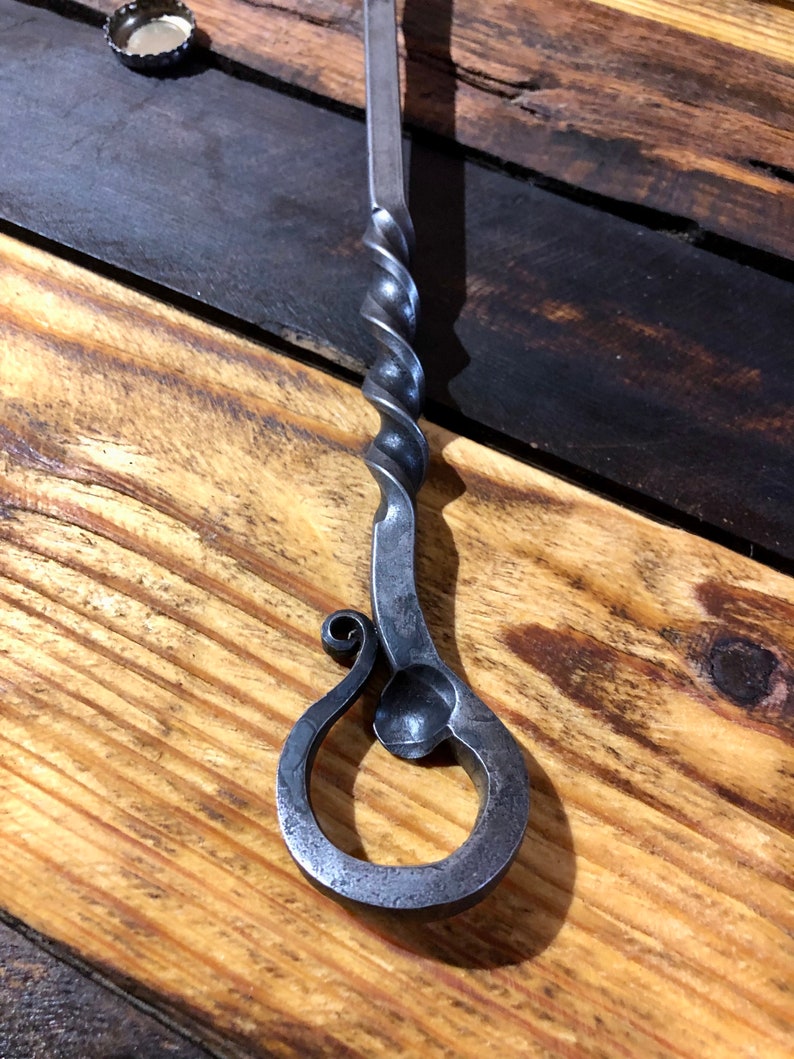 May include: A hand-forged bottle opener with a twisted metal handle and a decorative loop at the end.