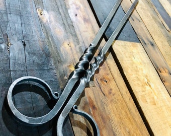 May include: A pair of black metal fireplace tongs with twisted handles and a loop at the end of each handle.