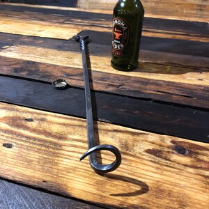 May include: A black metal fireplace poker with a curved handle. The poker is lying on a wooden surface. A bottle of Sonoma Cider is in the background.