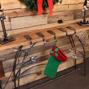 Può includere: Uno scaffale in legno con cinque ganci in metallo per appendere le calze. Una calza verde e rossa è appesa a uno dei ganci.